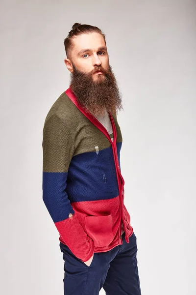 Ung bearded man tittar på kameran i studio i trendiga moderna färgade tröja med röd, mörk blå och Olivgröna ränder och blå chinos — Stockfoto