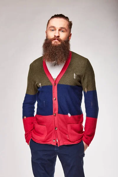 Joven barbudo posando en estudio en moderno suéter de color moderno con rayas rojas, azules oscuras y olivas y chinos azules —  Fotos de Stock