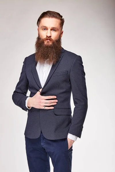Joven barbudo posando en estudio en blazer gris de moda, camisa blanca y pantalones azules —  Fotos de Stock