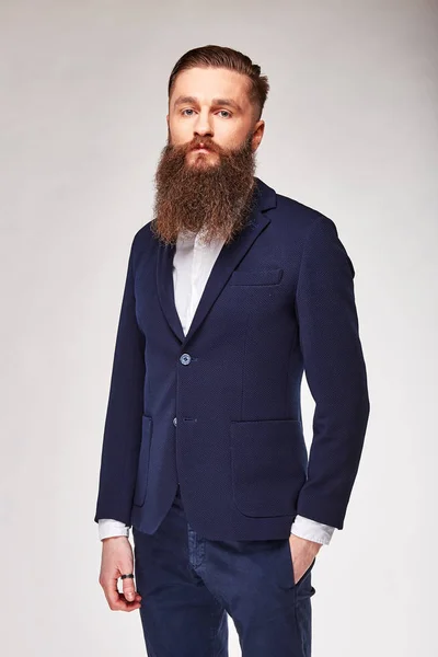 Молодий бородатий чоловік позує в студії в темно-синьому модному блістері, білій сорочці і синіх штанах — стокове фото