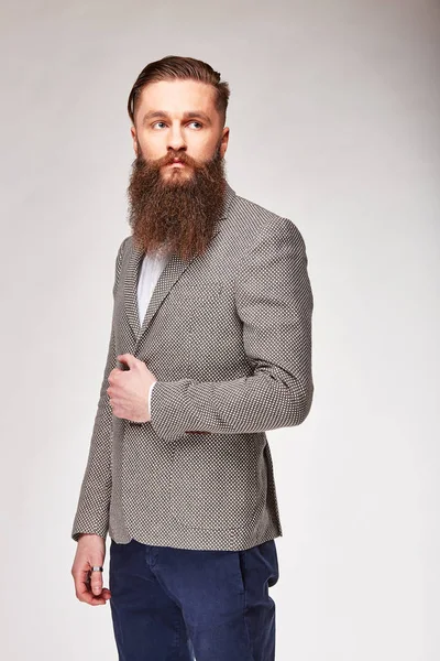 Joven barbudo posando en estudio en blazer gris de moda, camisa blanca y pantalones azules —  Fotos de Stock