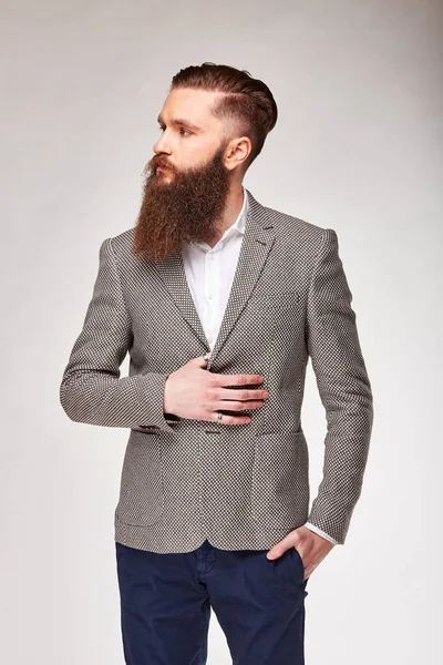 Young bearded man standing in studio in grey trendy blazer, white shirt and blue pants — Stock Photo, Image