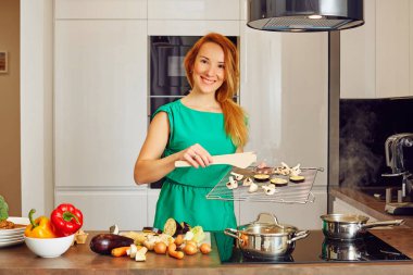 Yüksek teknoloji modern güneşli mutfak kamerada bakarak çok gülümseyen kadın Kızıl saçlı mutfak masasının duran ve ızgara sebzeler, holding