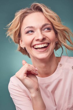 Studio turkuaz arka plan ile hafif pembe elbise giyen genç gülümseyen güzel sarışın kadın portresi