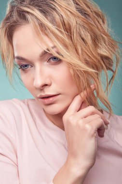 Portre portre Studio açık turkuaz renkli üzerinde hafif pembe elbise giyen genç ciddi romantik sarışın kadının iri gözlü ve dalgalı saçlı,