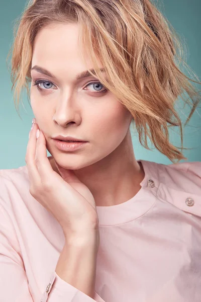 Potret close up dari wanita muda berambut pirang romantis yang serius dengan mata besar dan rambut bergelombang, mengenakan gaun merah muda ringan di studio dengan latar belakang pirus — Stok Foto