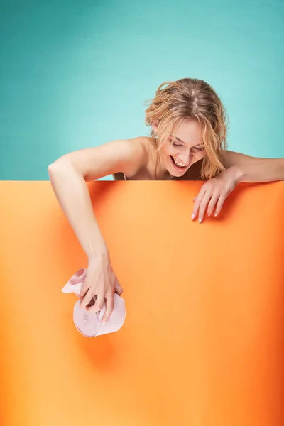 Νέοι όμορφη ξανθιά γυναίκα κρατώντας ρολό χαρτί τουαλέτας και γέλιο στο studio σε φόντο τιρκουάζ και πορτοκαλί φύλλο — Φωτογραφία Αρχείου