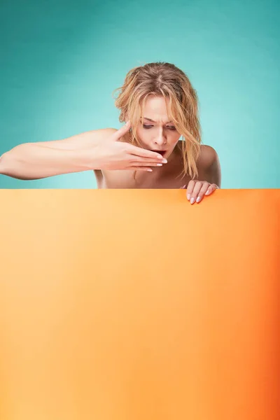 Young blonde woman posing in studio with turquoise background and orange sheet — Stock Photo, Image