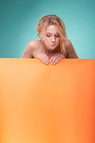 Mujer rubia linda joven mirando hacia abajo perturbado en el estudio con fondo turquesa y hoja de color naranja —  Fotos de Stock