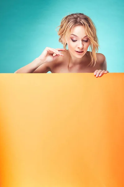 Νέοι χαριτωμένο ξανθιά γυναίκα κοιτάζοντας προς τα κάτω στο studio με φόντο τιρκουάζ και πορτοκαλί φύλλο — Φωτογραφία Αρχείου