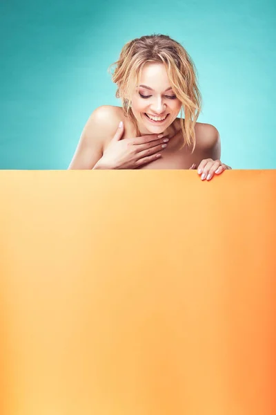 Young cute blonde woman looking down and smiling in studio with turquoise background and orange sheet — Stock Photo, Image