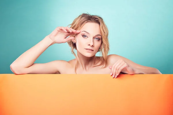 Jonge mooie blonde vrouw kijken camera in studio met turquoise achtergrond en oranje folie — Stockfoto