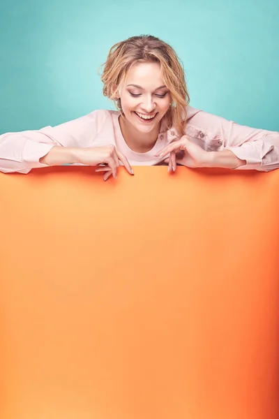 Joven linda mujer rubia riendo en el estudio con fondo turquesa y hoja naranja —  Fotos de Stock
