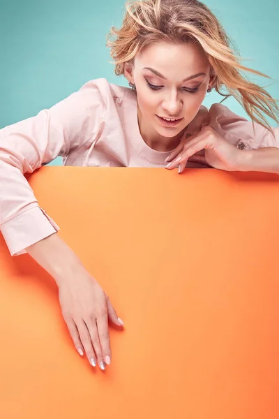 Retrato de la joven mujer rubia increíble mirando hacia abajo y quiere llegar a algo en el estudio con fondo turquesa y hoja naranja —  Fotos de Stock