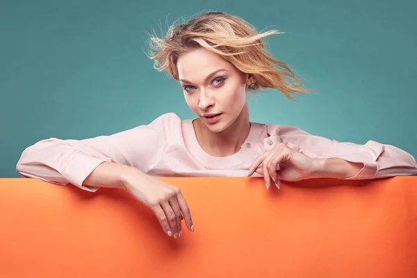 Retrato de una joven rubia guapa en vestido rosa claro mirando a la cámara con interés en el estudio con fondo turquesa y hoja naranja —  Fotos de Stock