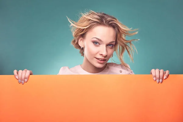 Retrato de mujer rubia bonita joven en vestido rosa claro mirando atento en el estudio con fondo turquesa y hoja naranja —  Fotos de Stock