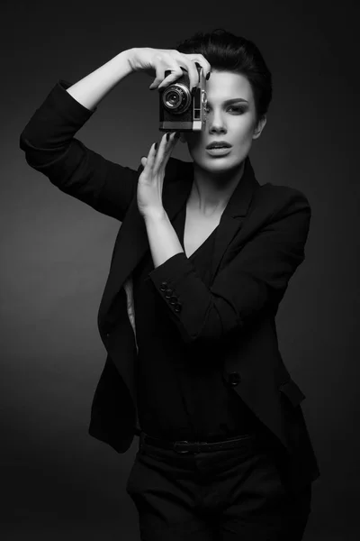 黒と白で、彼女の手で古い写真をカメラを持って、暗いスタジオでポーズをとって若いセクシーな女性カメラマン短い黒い髪を着て黒レトロなブレザー — ストック写真