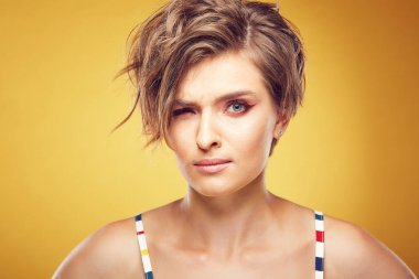 Seksi mutlu genç güzel kadın modeli kısa darmadağınık kahverengi saçlı ve ciddi bir yüz Studio Sarı zemin üzerine poz, closeup portresi