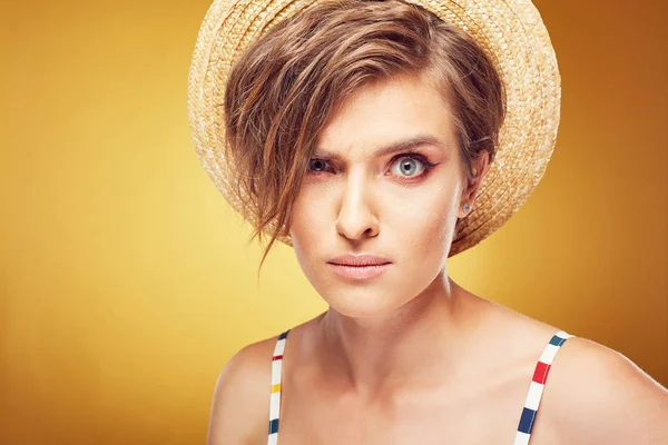 Closeup portrait of sexy young pretty woman with short disheveled brown hair, looking serious, wearing straw hat, posing in studio on yellow background — Stock Photo, Image