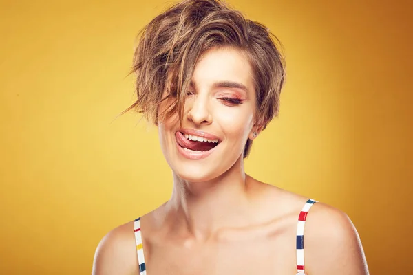 Closeup πορτρέτο της σέξι ευτυχισμένη νεαρές αρκετά μοντέλο με κοντό αναμαλλιασμένος καστανά μαλλιά, με κλειστά μάτια, πλατύ χαμόγελο και έδειξε γλώσσα, θέτοντας στο studio σε κίτρινο φόντο — Φωτογραφία Αρχείου