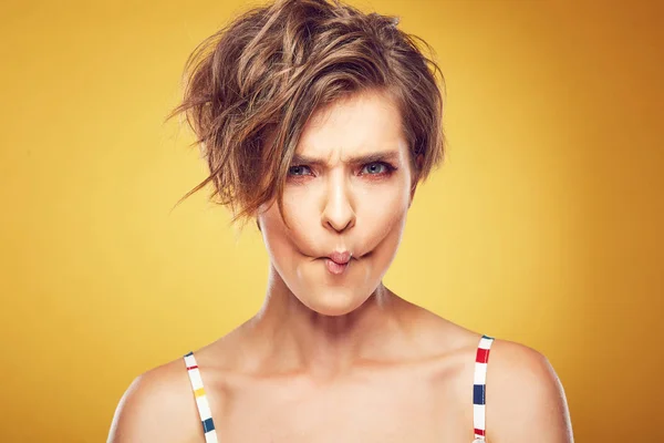 Closeup portrait of sexy happy young pretty female model with short disheveled brown hair, and funny face, posing in studio on yellow background — Stock Photo, Image