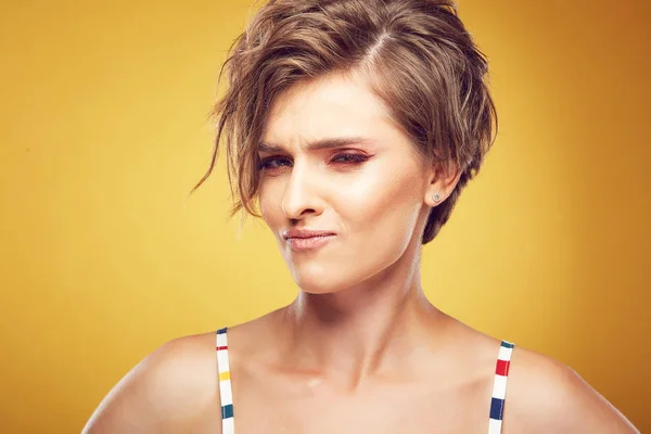 Closeup portrait of sexy happy young pretty female model with short disheveled brown hair, and sly face, posing in studio on yellow background — Stock Photo, Image