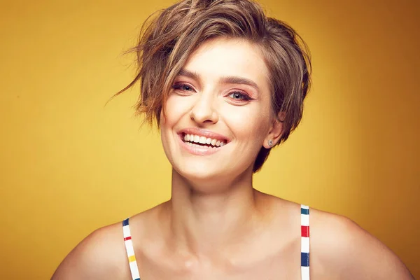 Closeup portrait of sexy happy young pretty female model with short disheveled brown hair, and happy smiling face, posing in studio on yellow background — Stock Photo, Image