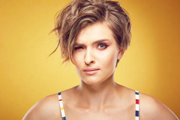 Closeup portrait of sexy happy young pretty female model with short disheveled brown hair, and serious face, posing in studio on yellow background — Stock Photo, Image