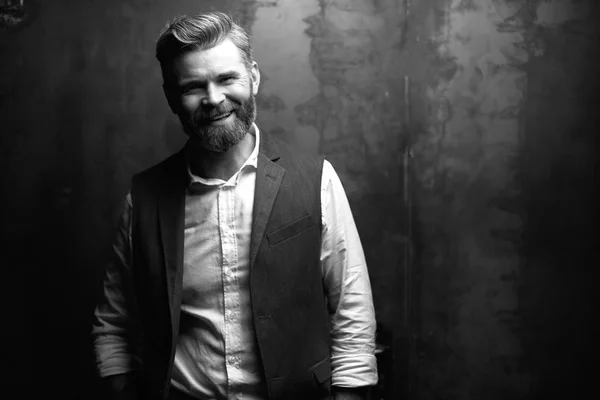 Stilig leende man med skägg, klädd i vit skjorta och svart väst, står i studion på mörk grå bakgrund — Stockfoto