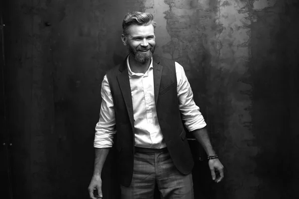 Bello uomo sorridente con la barba, con camicia bianca e gilet nero, in posa in studio su sfondo grigio scuro — Foto Stock