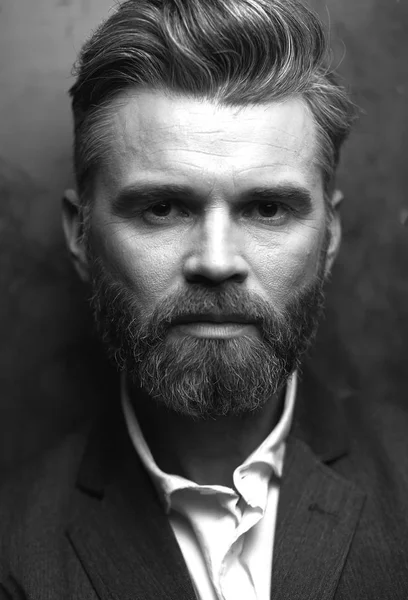 Крупный план портрета красивого красивого серьезного человека с бородой, в белой рубашке и черном жилете, позирующего в студии на темно-сером фоне в черно-белом — стоковое фото