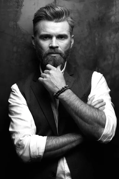 Відмінний портрет красивого серйозного чоловіка з бородою, в білій сорочці і чорному жилеті, позує в студії на темно-сірому тлі в чорно-білому — стокове фото
