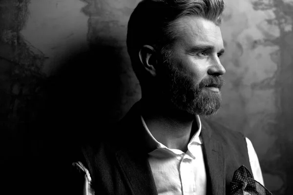 Відмінний портрет красивого серйозного харизматичного чоловіка з бородою, в білій сорочці і чорному класичному жилеті, позує в студії на темно-сірому фоні, в чорно-білому — стокове фото