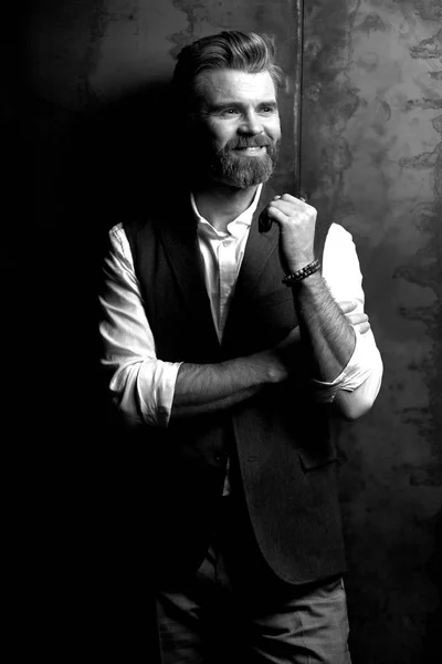 Портрет гарного усміхненого чоловіка з бородою, в білій сорочці і чорному класичному жилеті, позує в студії на темно-сірому тлі, чорно-білому — стокове фото