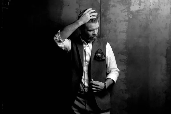 Гарний серйозний харизматичний чоловік з бородою, в білій сорочці і чорному класичному жилеті, позує в студії на темно-сірому тлі, чорно-білому — стокове фото