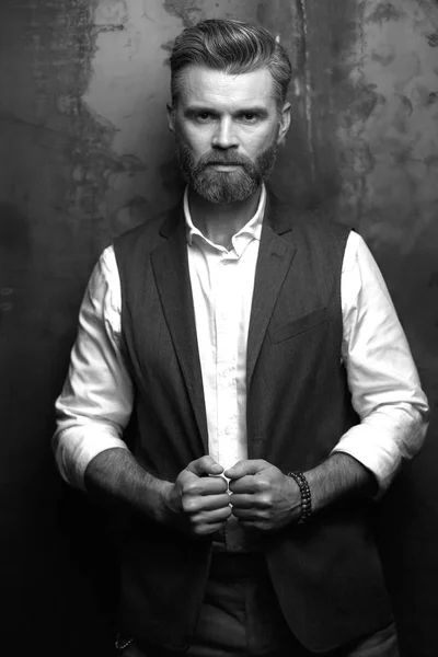 Jóképű férfi szakállal, fehér inget és fekete klasszikus mellény, pózol stúdió sötét szürke háttér, fekete-fehér portré — Stock Fotó