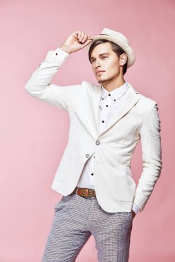 Beyaz ceket, beyaz gömlek, gri pantolon ve Studio açık pembe renkli ile poz ve şapkasını dokunmadan beyaz şapka giyen genç güzel mutlu ciddi modern erkek modeli