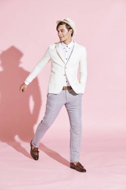 Genç güzel ciddi modern adam beyaz ceket, beyaz gömlek, gri pantolon ve beyaz şapka ile açık pembe renkli studio ile adım