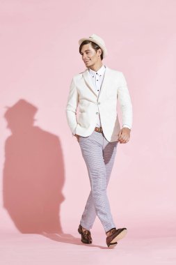Genç güzel ciddi modern adam beyaz ceket, beyaz gömlek, gri pantolon ve beyaz şapka Studio açık pembe renkli ile poz