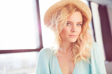 Turkuaz elbiseyi, bileziği ve güneşli Studio doğal ışık ışık şapka poz giyen genç sarışın seksi güzel ciddi kadın uzun kıvırcık saçlı closeup portresi