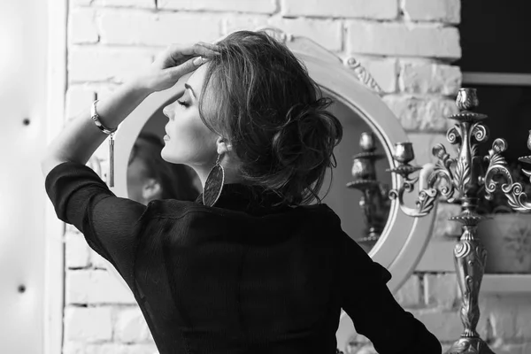 Портрет молодой привлекательной брюнетки с гламурным макияжем, сидящей у зеркала в черно-белом — стоковое фото
