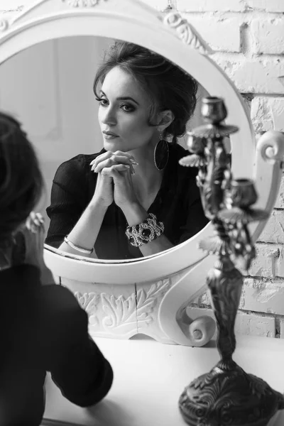 Портрет молодої привабливої брюнетки ніжної жінки з гламурним макіяжем, одягнений в чорну глибоконогу блузку і легку спідницю, дивлячись і позуючи біля круглого білого дзеркала, в чорно-білому — стокове фото