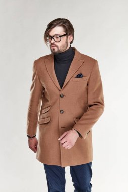 Sakal ve gözlük hafif kahverengi kaşmir palto ve koyu mavi pantolon Işık Studio poz ile çekici genç seksi erkek modeli 