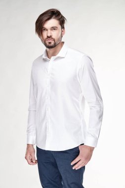 Çekici bir genç adam modeli sakallı ve siyah saçlı beyaz gömlek ve koyu mavi pantolon Işık Studio poz ile