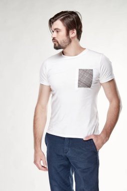 Çekici bir genç adam modeli sakallı ve siyah saçlı beyaz tshirt gri cep ve koyu mavi pantolon Işık Studio ile poz ile