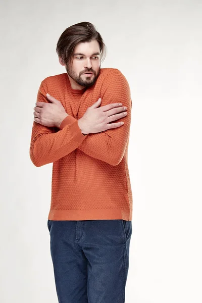 Atrakcyjne młody człowiek sexy model z brodą i ciemne włosy pozowanie w pomarańczowy sweter i ciemne spodnie niebieskie światła Studio — Zdjęcie stockowe