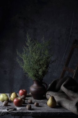 Ceviz, armut, elma ve sürahi ile yeşil bitkilerde, karanlık Studio ahşap masa üzerinde büyük natürmort