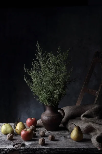 Ceviz, armut, elma ve sürahi ile yeşil bitkilerde, karanlık Studio ahşap masa üzerinde büyük natürmort
