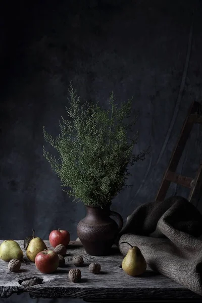 Ceviz, armut, elma ve sürahi ile yeşil bitkilerde, karanlık Studio ahşap masa üzerinde büyük natürmort