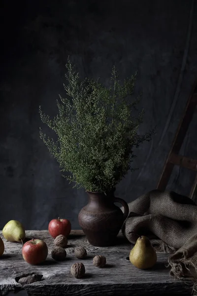 Güzel natürmort ceviz, armut, elma ve sürahi ile karanlık Studio ahşap masa üzerinde yeşil bitkiler